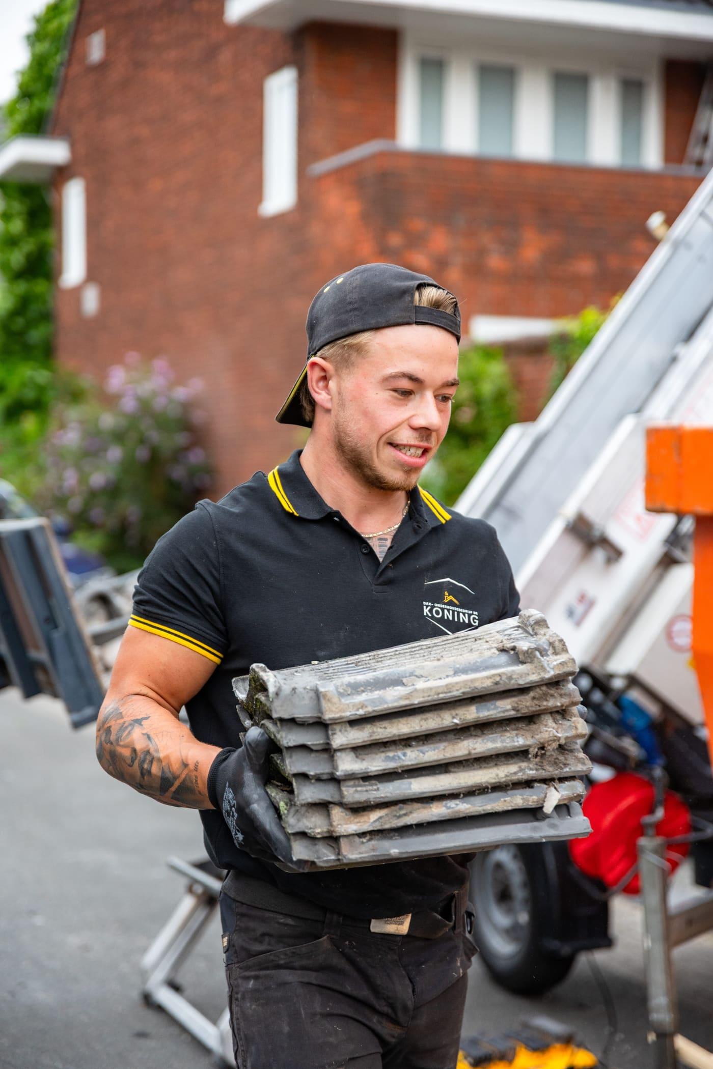 Vakman van De Koning draagt nieuwe dakpannen naar het dak in Utrecht